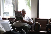 Man with newspaper, Mahè Airport, by marcorossimusic